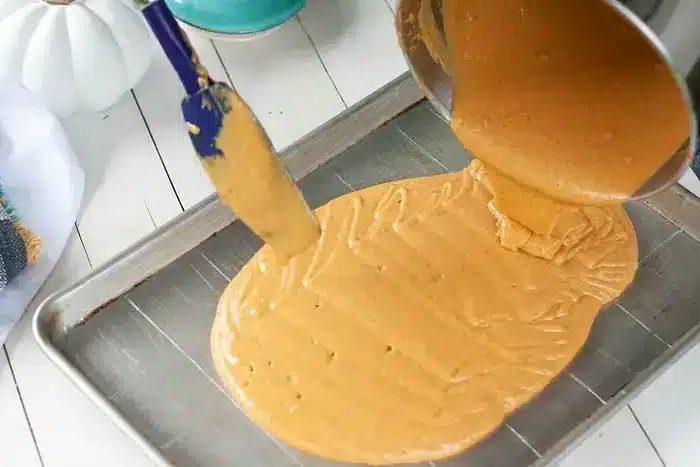 A thick, caramel-colored mixture is being poured from a pot onto a large metal baking sheet, solid for creating a delightful 1/2 sheet cake.