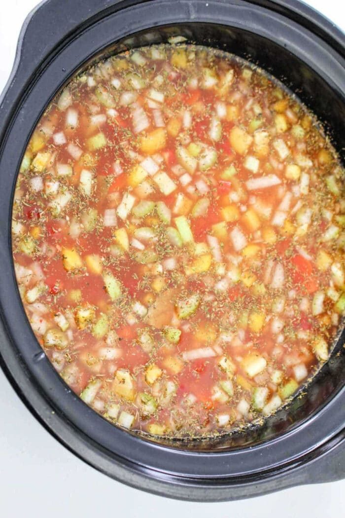 Chopped vegetables and broth in a slow cooker, solid for making a hearty 15 Bean Soup Crock Pot recipe.