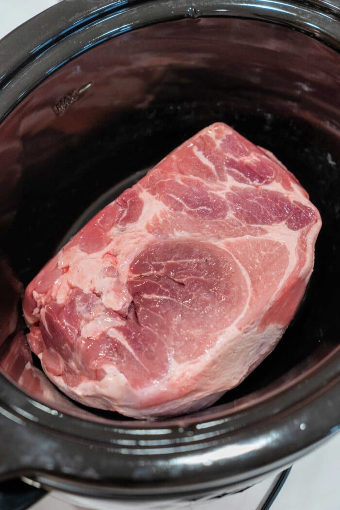 A large raw pork roast set inside a slow cooker is the solid start to an easy pulled pork recipe.