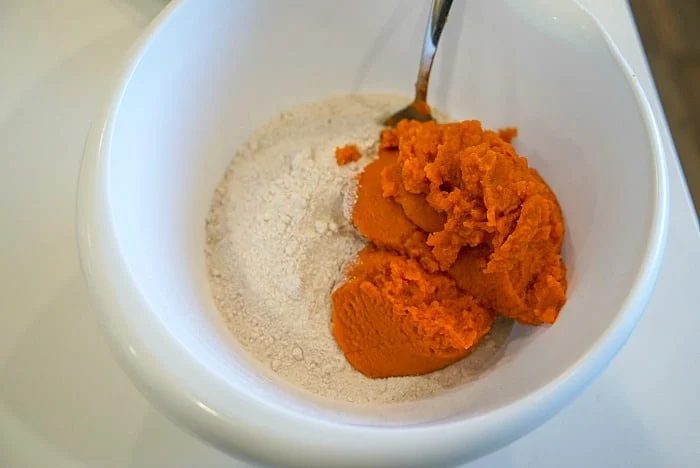 A white bowl holds a simple mix of cake mix and vibrant orange pumpkin puree, with a metal spoon ready to stir. solid for crafting fluffy 2-ingredient pumpkin muffins.