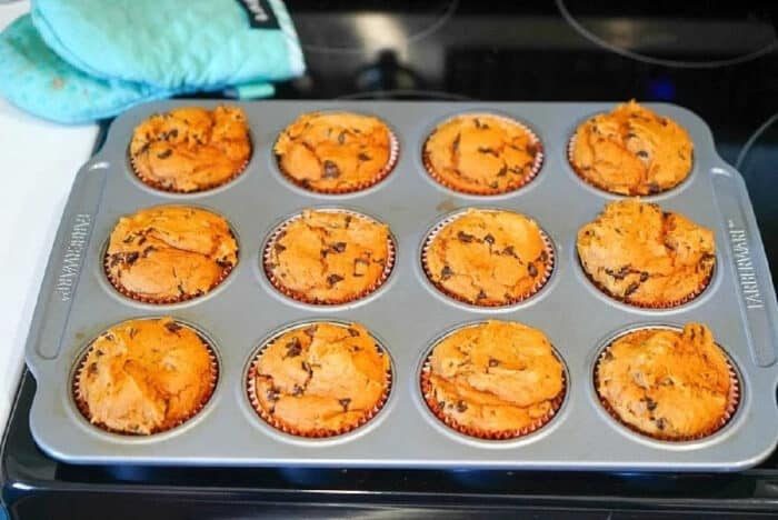 A tray of freshly baked 2 ingredient pumpkin muffins, rests on the stovetop with an oven mitt nearby.