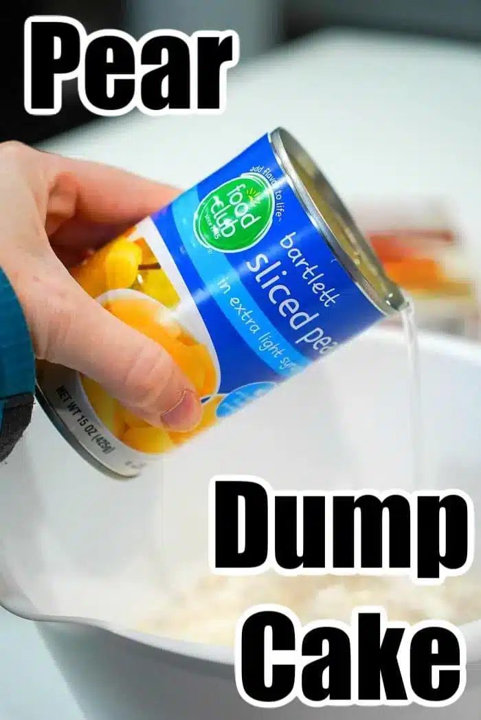 A hand is pouring a can of sliced pears in extra light syrup into a white mixing bowl. The can has a blue label with an image of pears.