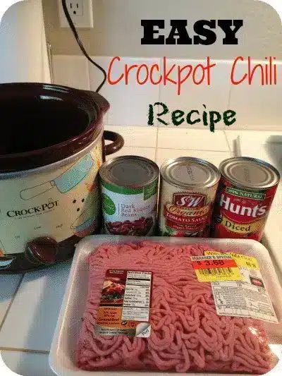 Image of a kitchen counter with ingredients for a 5 ingredient crockpot chili recipe. A crockpot is next to three cans (light red kidney beans, tomato sauce, diced tomatoes) and a package of ground beef.