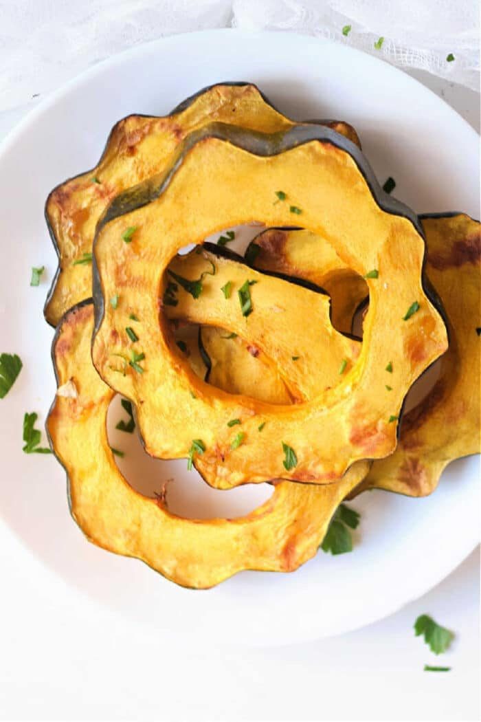 Three roasted acorn squash rings, prepared in the air fryer, are garnished with chopped herbs on a white plate.