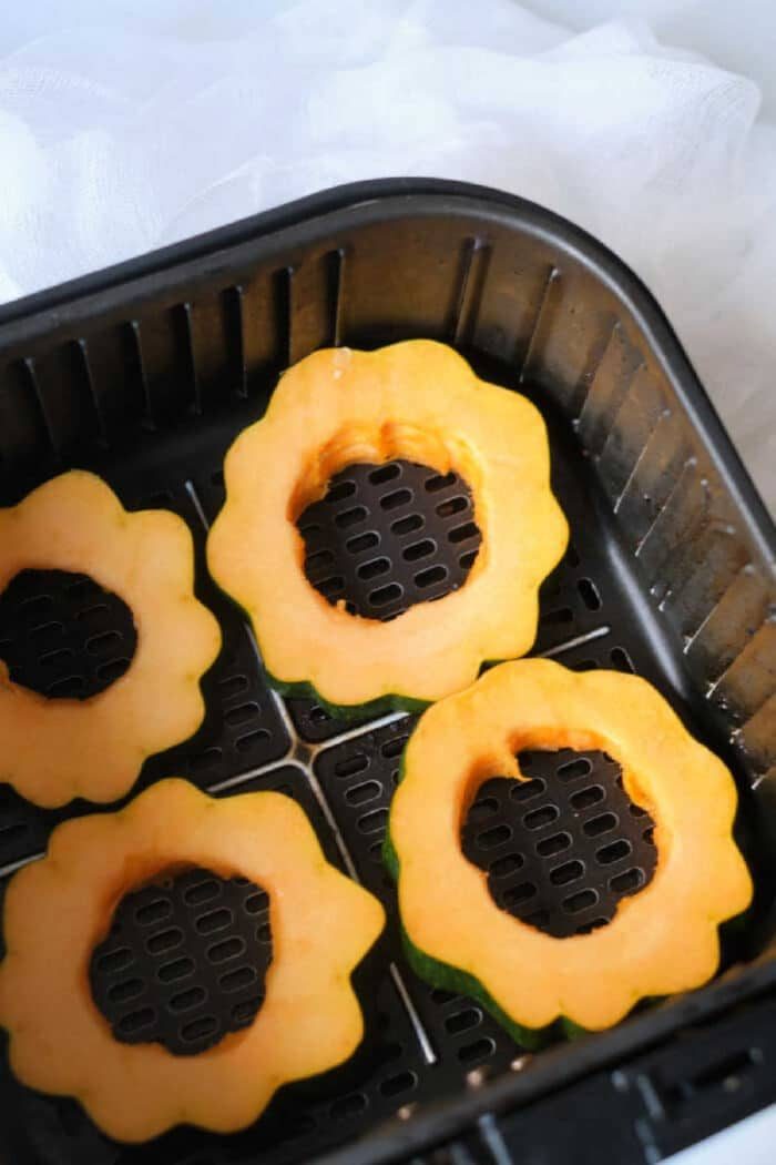 Four raw air fryer acorn squash rings are arranged in the basket, ready to be cooked to perfection.