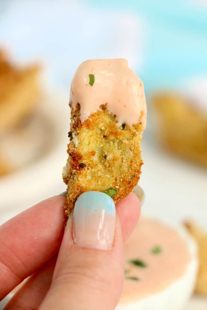 Close-up of a hand holding a breaded perfectly cooked air fryer artichoke hearts.