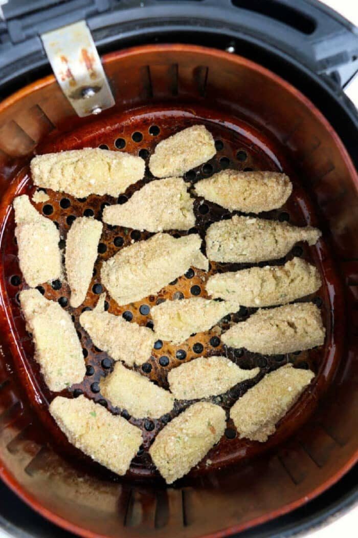 Breaded zucchini slices arranged in a single layer inside an air fryer basket, ready to be cooked—solid alongside air fryer artichoke hearts for a tasty appetizer spread.