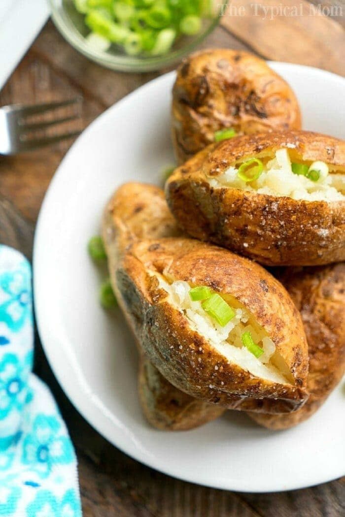 Air fryer baked potatoes on a white plate, split open and topped with chopped green onions.