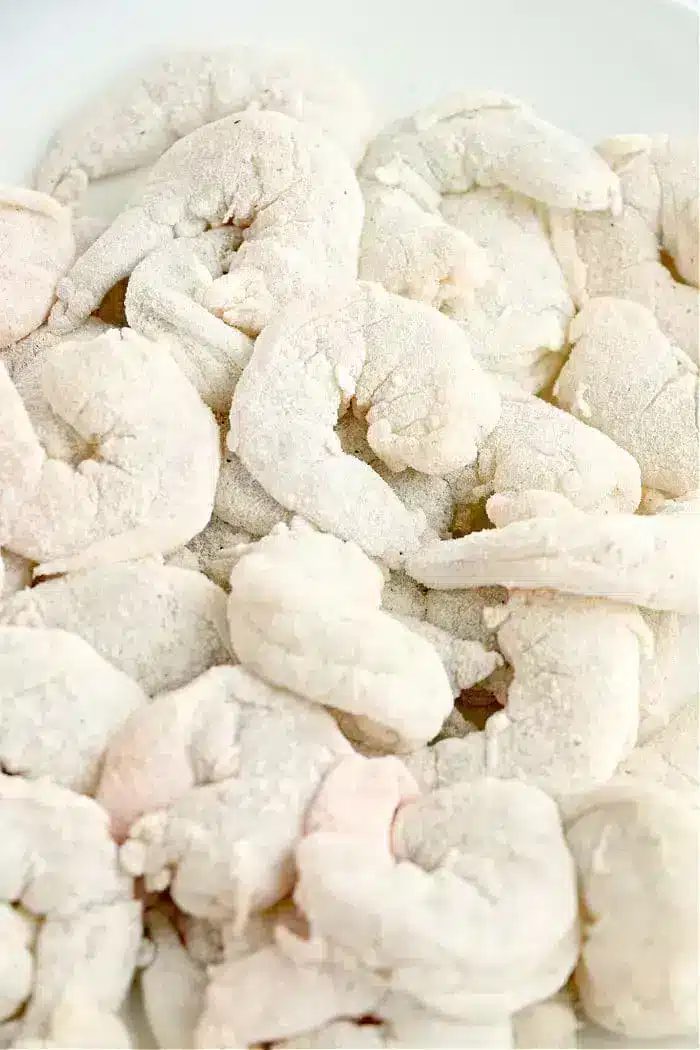 Frozen, uncooked shrimp piled together, covered in a light layer of frost on a white surface—solid for making crispy air fryer bang bang shrimp at home.