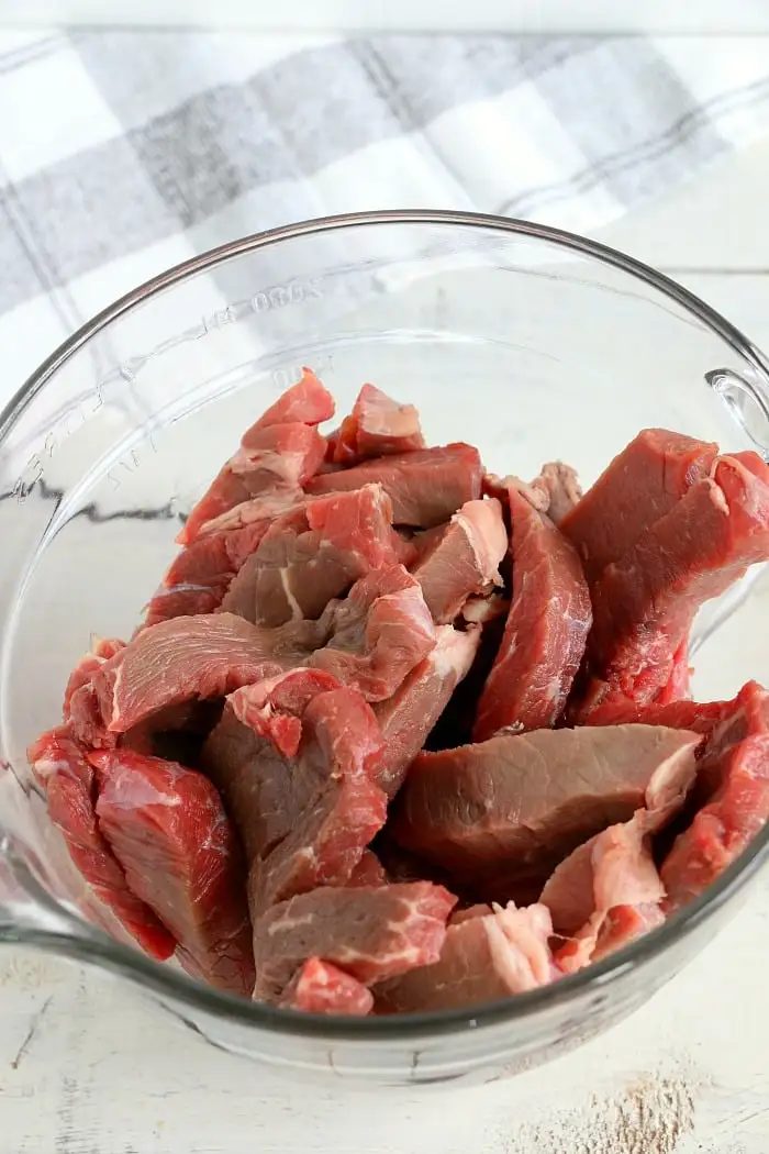 A clear glass bowl filled with raw, thinly sliced beef pieces, solid for making air fryer beef jerky.