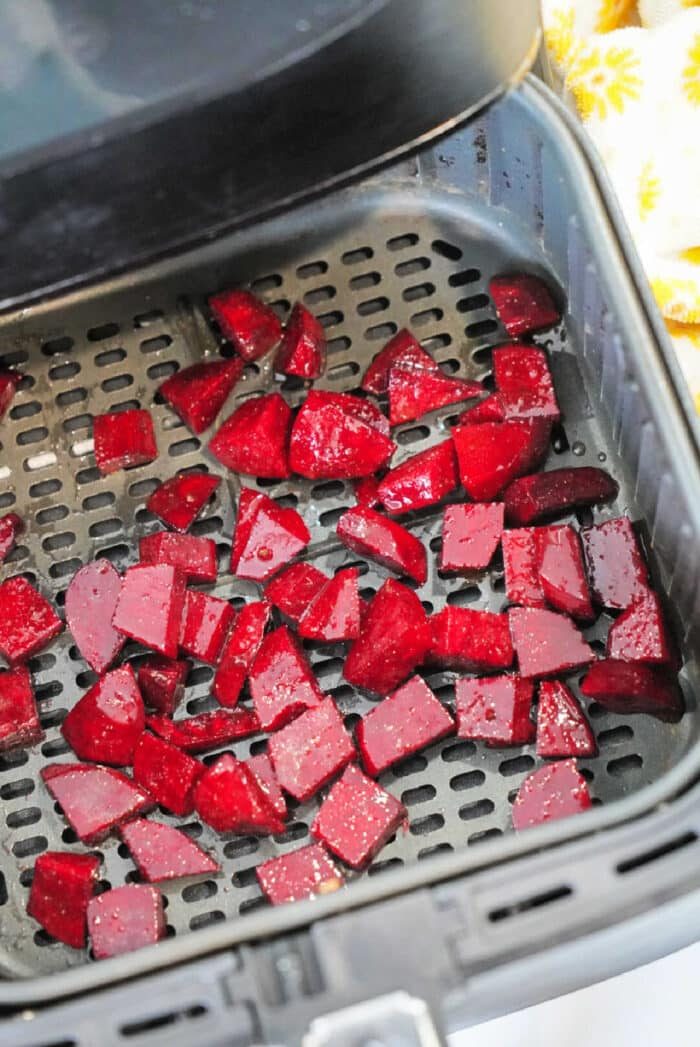 Diced red beets placed in an air fryer basket, ready for cooking. These air fryer beets are spread out evenly across the perforated surface.