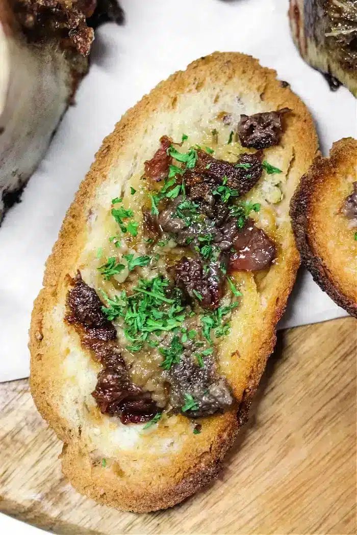 A slice of toasted bread topped with chopped beef and rich bone marrow, garnished with finely chopped parsley, displayed on a wooden surface.