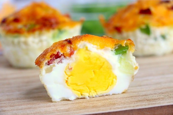 A close-up of halved air fryer egg muffin bites reveals a vibrant yolk, gooey cheese, and colorful vegetable pieces, all resting enticingly on a wooden surface.