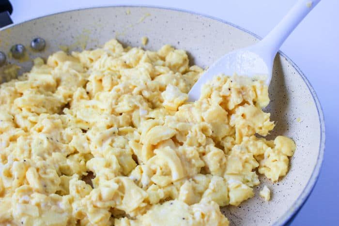 Scrambled eggs sizzle in a frying pan, a white spatula stirring them to perfection—a morning symphony for the solid breakfast burrito.