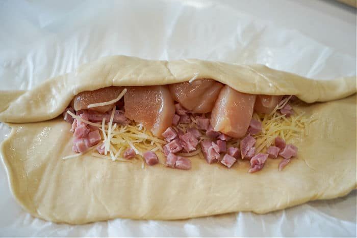 Unbaked pastry filled with diced chicken, grated cheese, and chicken pieces awaits transformation into a good air fryer chicken cordon bleu on parchment paper.