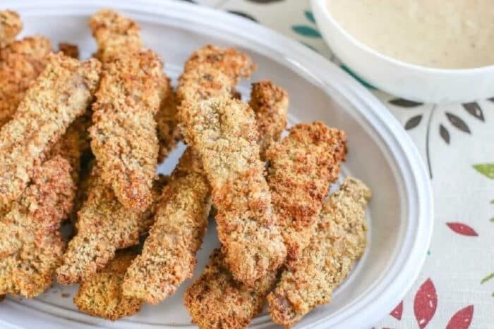 A plate of crispy breaded zucchini fries with a bowl of dipping sauce on the side, served alongside air fryer chicken fried steak for a good comfort food combo.