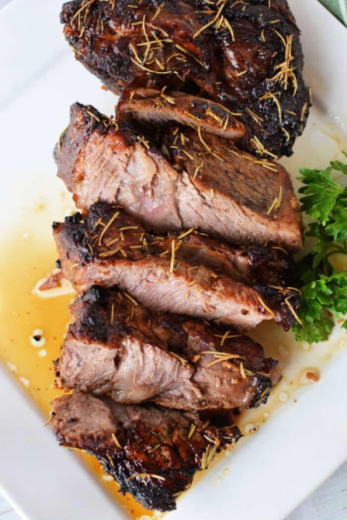 Sliced, juicy grilled beef steak with herbs on a white plate, garnished with fresh parsley—perfectly tender, like an air fryer chuck roast.