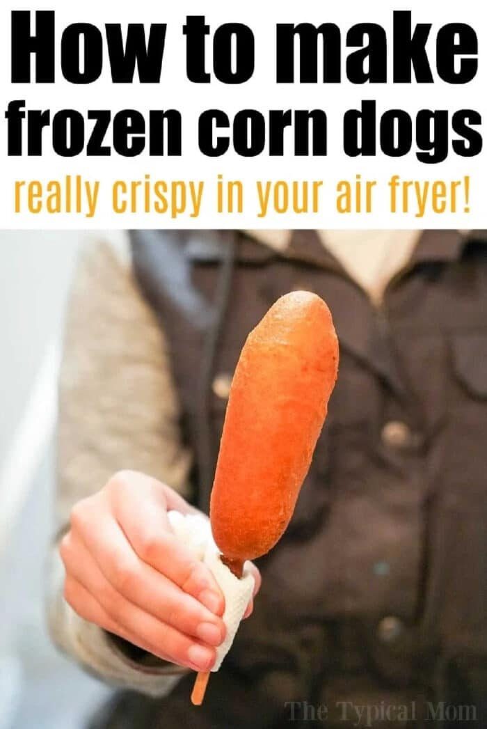 A person holding a corn dog with a napkin, with text about making crispy frozen air fryer corn dogs.