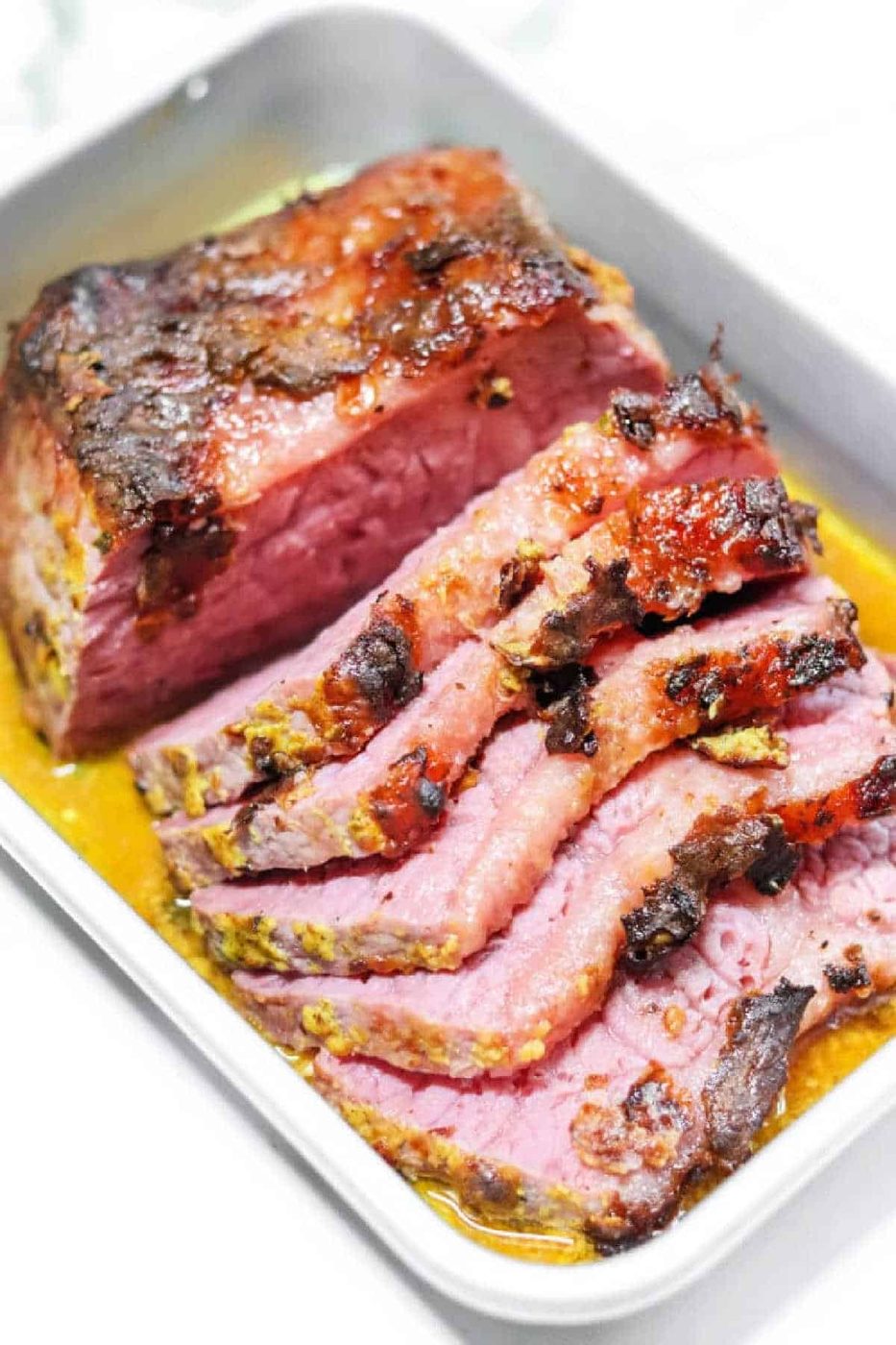 Sliced, glazed Air Fryer Corned Beef brisket in a white baking dish with some juices.