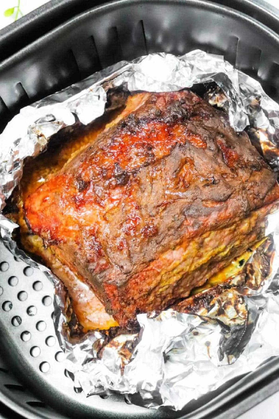 Cooked Air Fryer Corned Beef resting on crumpled aluminum foil inside an air fryer basket.
