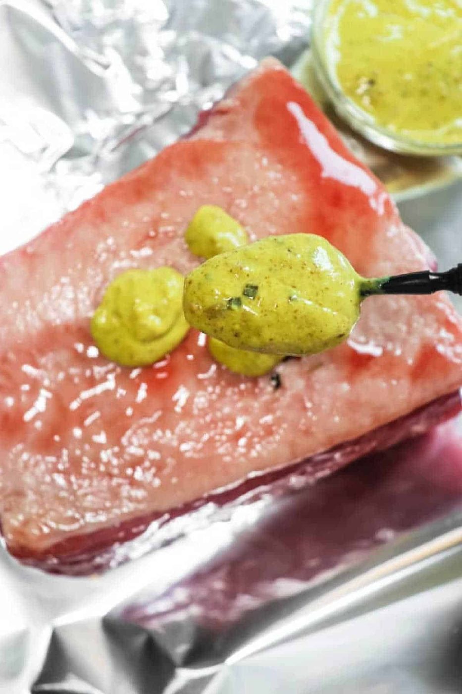 A spoon spreads yellow mustard sauce onto a raw corned beef brisket on aluminum foil, solid for making Air Fryer Corned Beef.