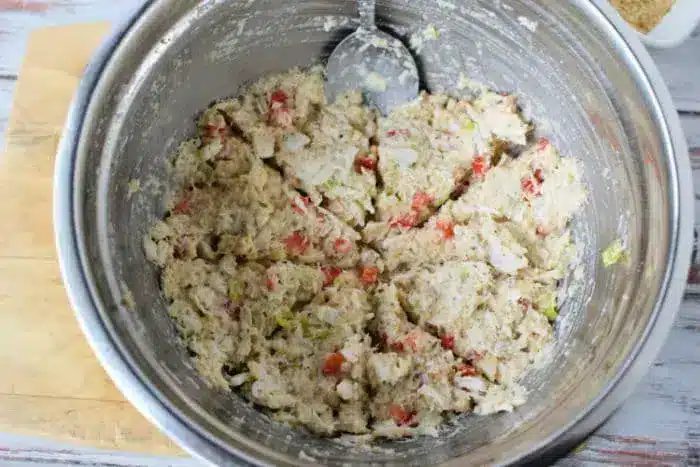 A metal mixing bowl containing a mixture of various chopped ingredients, likely including bread crumbs, bits of red and green vegetables, and a creamy binder for Air Fryer Crab Cakes.