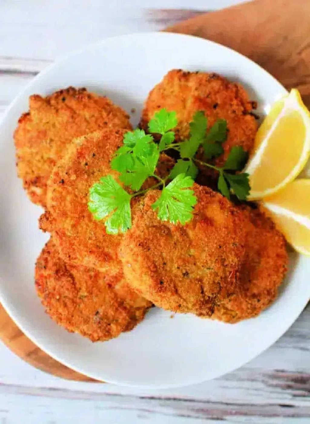 Five golden brown Air Fryer Crab Cakes garnished with cilantro and lemon wedges on a white plate.