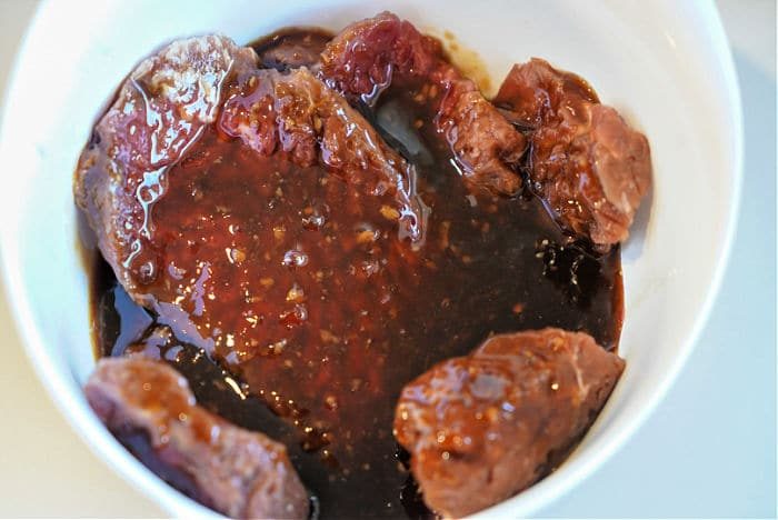 Raw cube steak pieces marinating in a dark, thick sauce in a white bowl, solid for an air fryer feast.