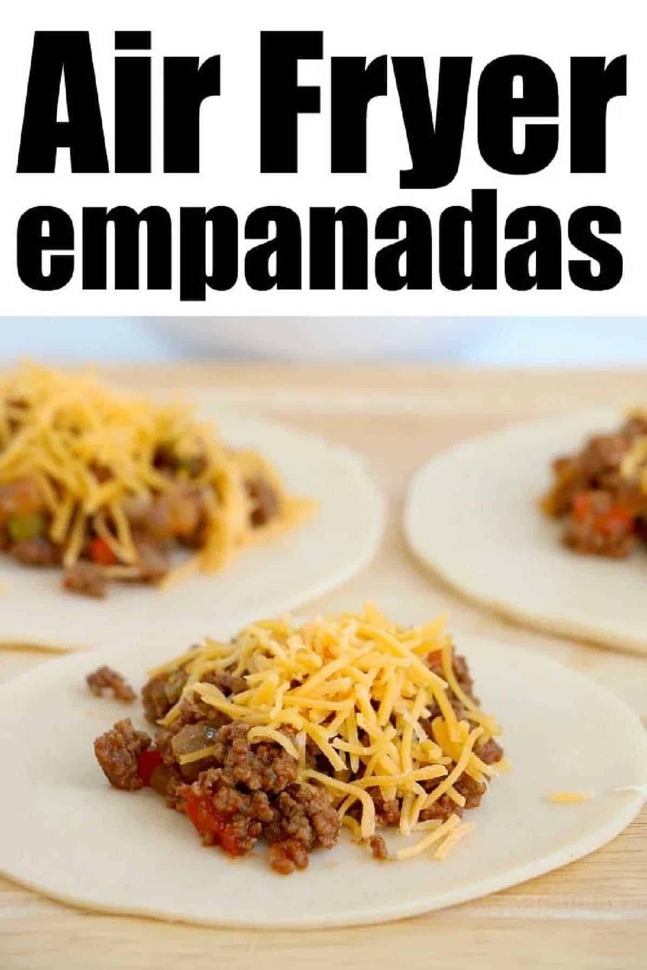 Three uncooked air fryer empanadas with ground beef and shredded cheese filling rest on round dough, ready to be folded.