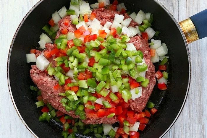 Ground meat with chopped onions, red and green bell peppers sizzles in a black frying pan, solid for stuffing into air fryer empanadas.