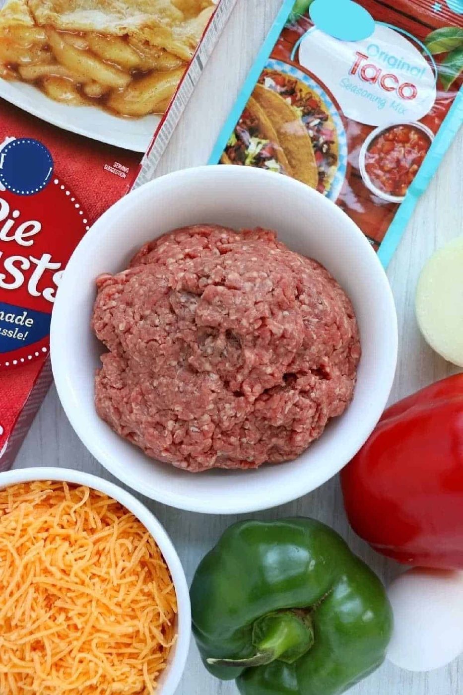 Ground beef in a white bowl with pie crusts, taco seasoning, cheese, onion, and peppers nearby—solid for making air fryer empanadas at home.