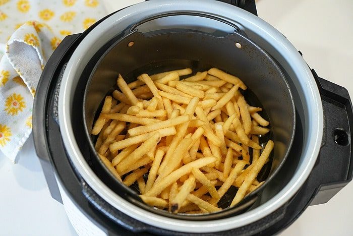 Crispy French fries sit beside a yellow floral cloth, freshly golden from the air fryer. Perfectly paired with good ninja foodi fish and chips for a delightful meal.