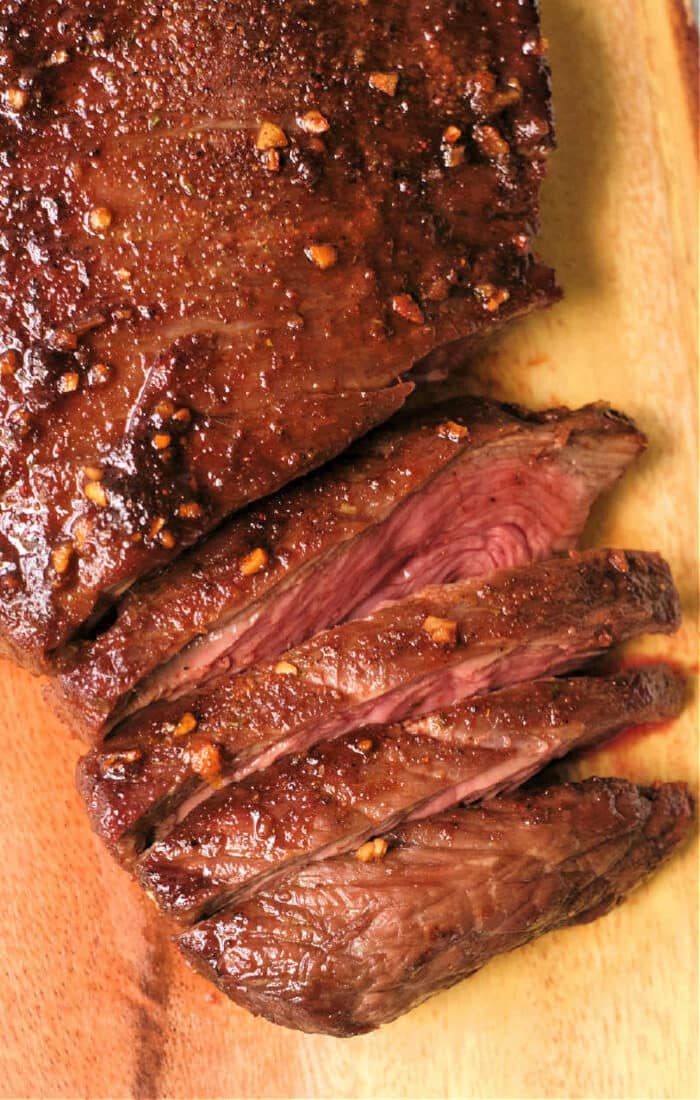 Sliced, juicy flank steak with a seared crust and garlic seasoning sits elegantly on a wooden cutting board, reminiscent of perfectly cooked air fryer flank steak.