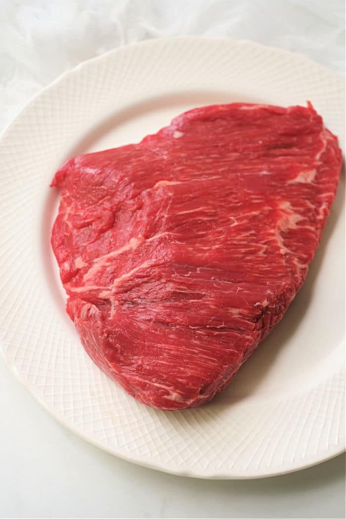 A raw flank steak rests invitingly on a white plate, waiting to be transformed into a succulent dish in the air fryer.