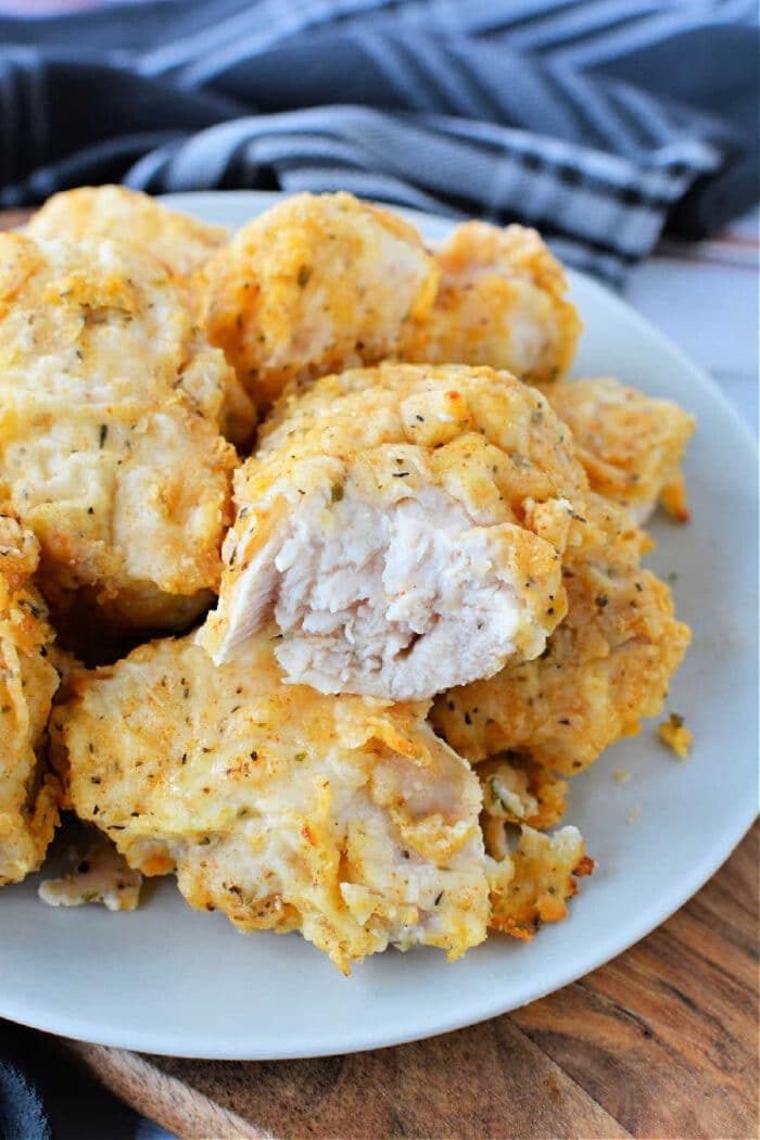 A plate of golden, crispy air fryer fried chicken breast bites with one piece revealing the juicy inside.