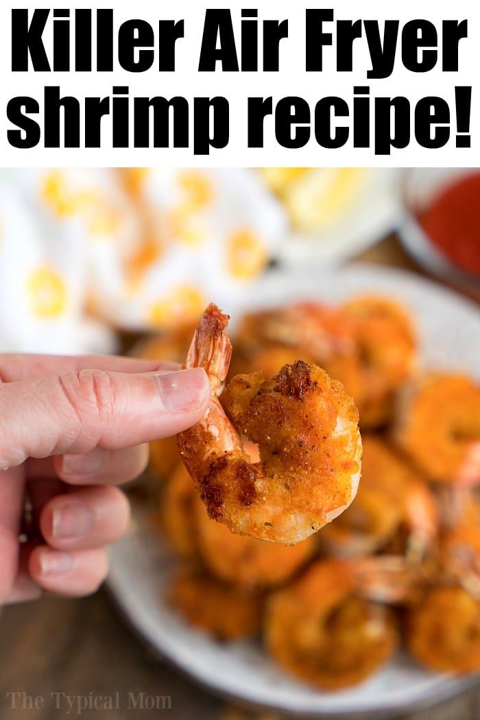 A hand holds a piece of crispy shrimp, with more air fryer fried shrimp on a plate in the background. Bold text at the top reads, Killer Air Fryer shrimp recipe!
