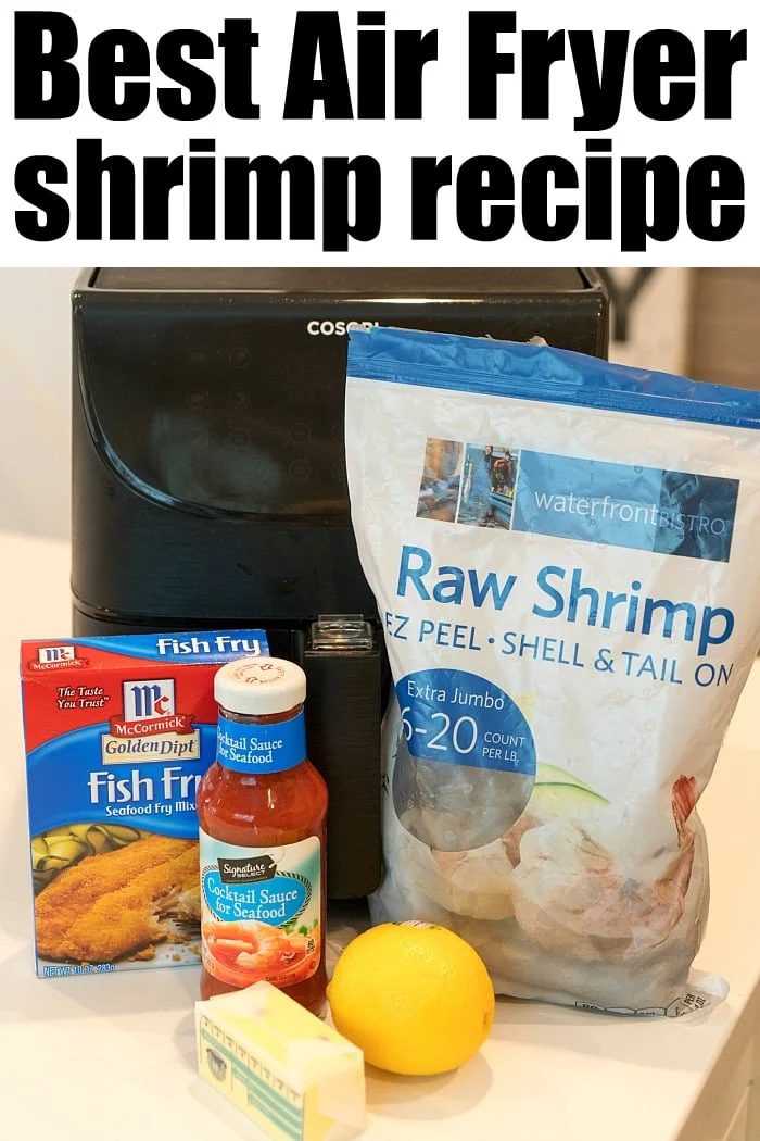 An air fryer sits on a countertop surrounded by ingredients for good fried shrimp: a bag of raw shrimp, fish fry seasoning, cocktail sauce, lemon, and butter. Text reads Best Air Fryer Fried Shrimp Recipe.