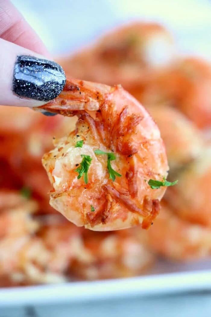 A hand with black glittery nails holds a cooked shrimp garnished with herbs, freshly made from air fryer frozen shrimp.