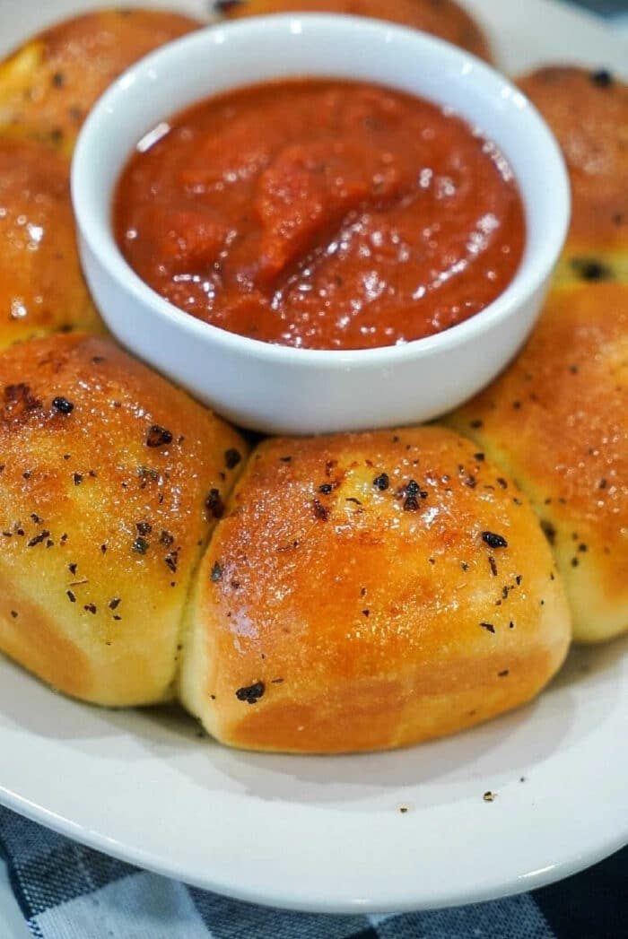 Golden baked Frozen Rolls in Air Fryer surround a bowl of marinara sauce on a white plate.