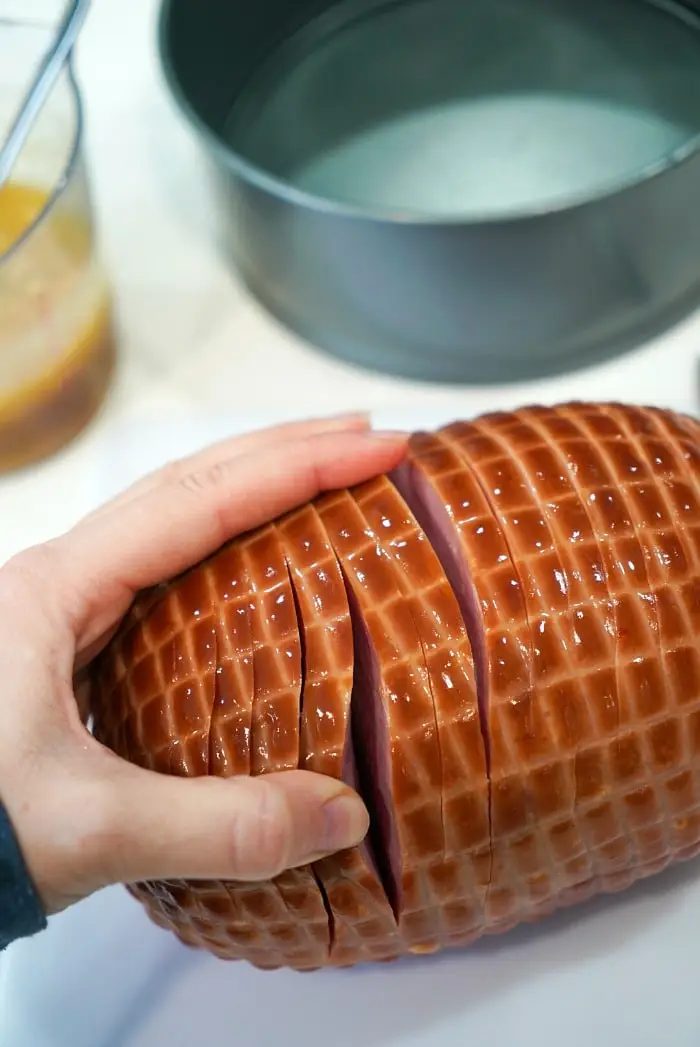 A hand slices an air fryer ham with a grid pattern on its surface.
