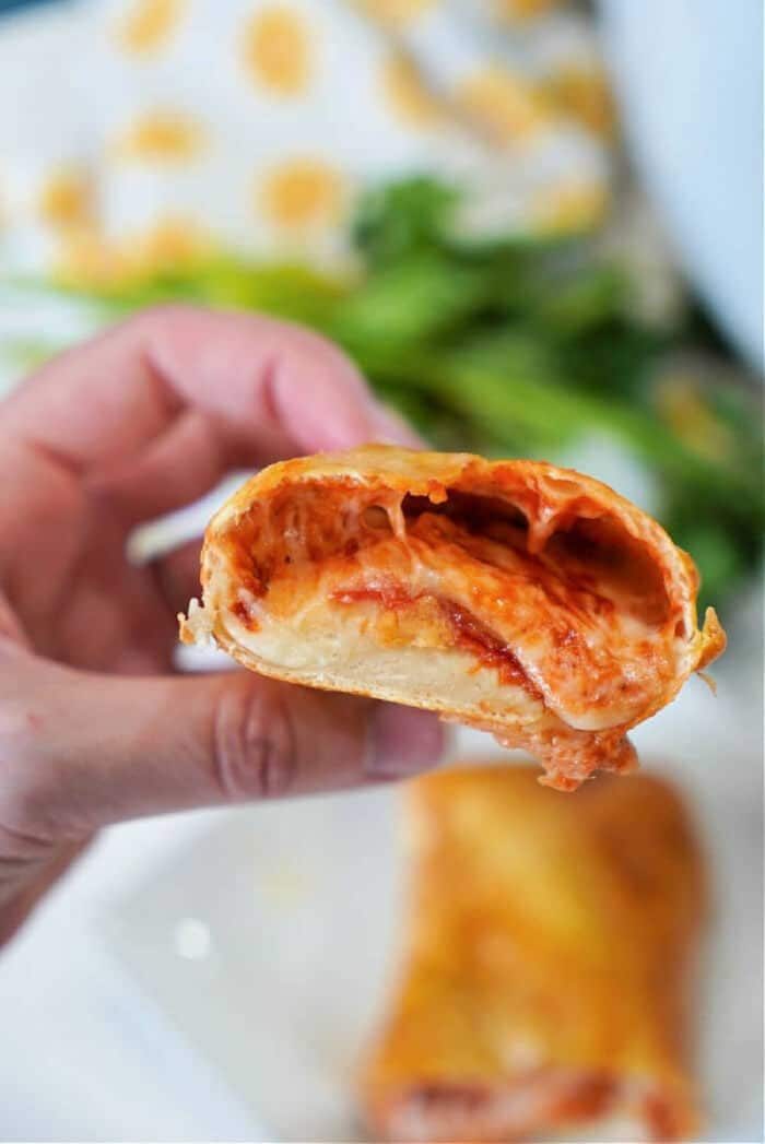 A hand holds a cheesy, sauce-filled pizza roll with a bite taken out of it—like fresh air fryer hot pockets, crispy on the outside and melty inside.