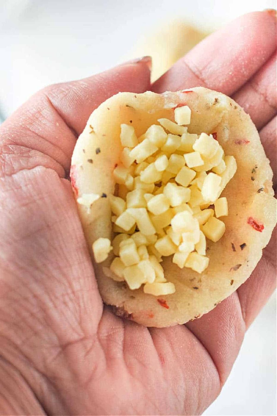 A hand holds mashed potatoes filled with small cubes of cheese, ready to be baked—solid as a side for Air Fryer Mashed Potato Balls.