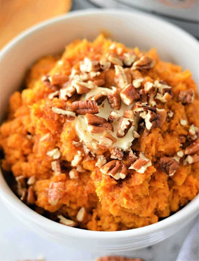 Mashed sweet potatoes topped with chopped pecans and a pat of melting butter in a white bowl—an easy twist on classic air fryer mashed potatoes.