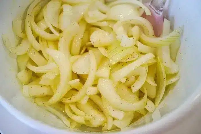 A close-up image of sliced onions in a white bowl, seasoned with a light sprinkling of salt and pepper after being perfectly crisped in the air fryer.