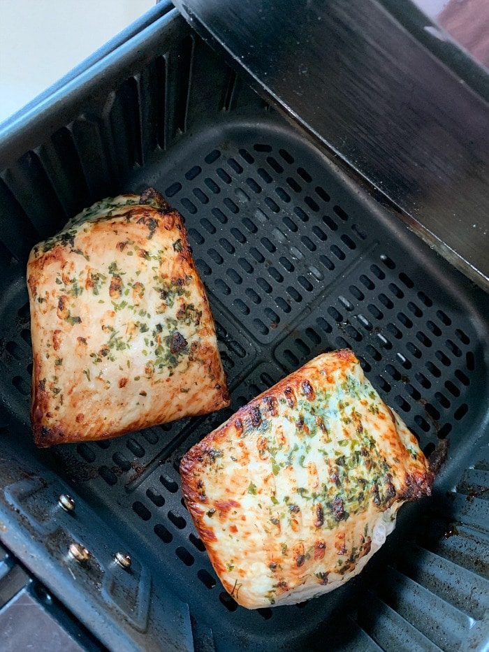 Two seasoned pork fillets sit in an air fryer basket, lightly browned and sprinkled with herbs. For a hearty twist, use this method to prepare an air fryer pork loin as well.