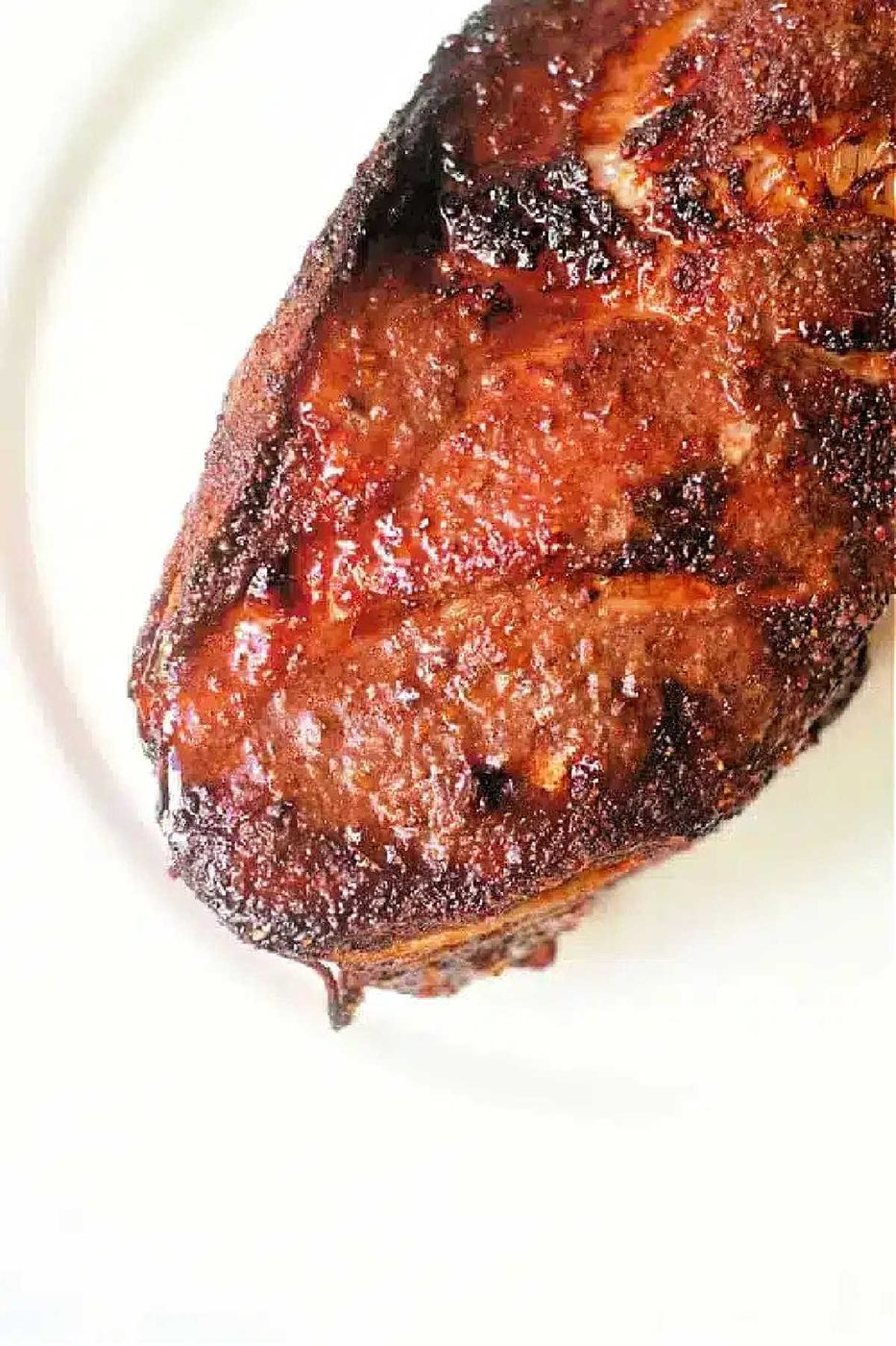 Close-up of a cooked, well-seasoned steak with a crispy, caramelized crust on a white plate, reminiscent of the solid finish an air fryer pork roast offers.