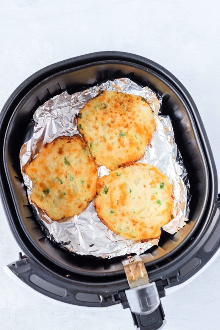 Golden-brown and crispy, these air fryer potato pancakes rest perfectly on foil in the basket, showcasing a delightful blend of flavors.
