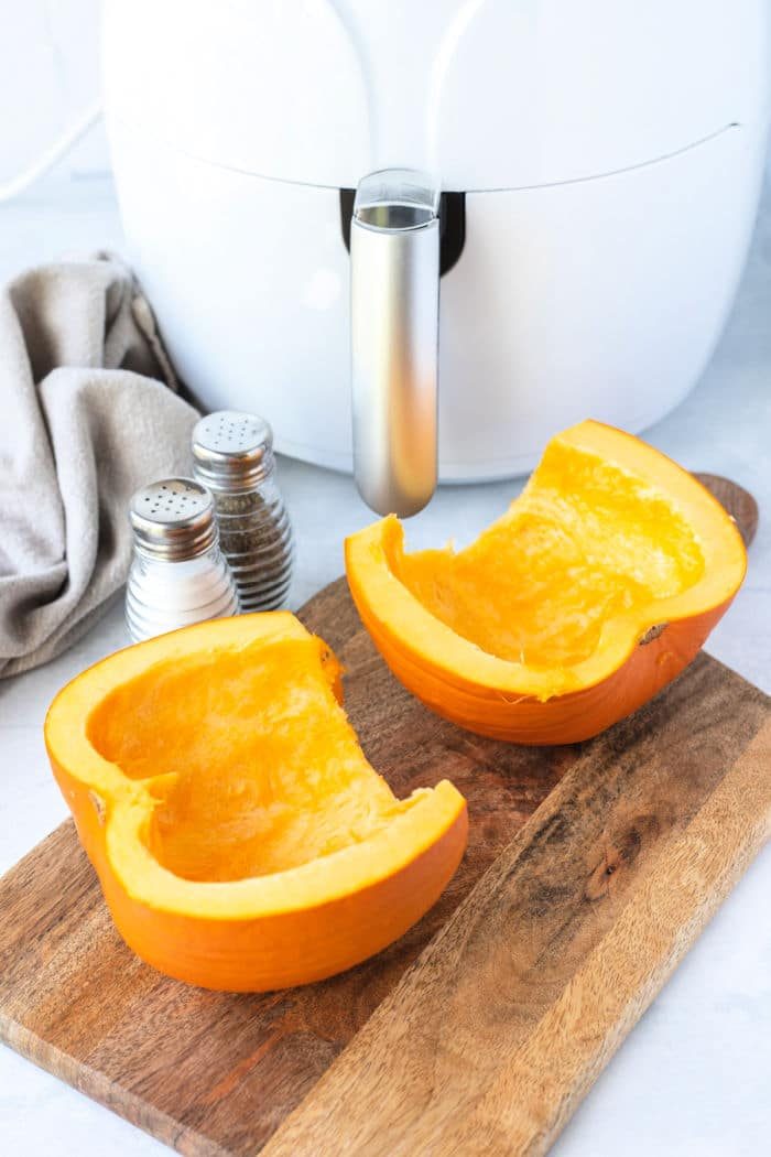 Two pumpkin halves rest on a wooden cutting board beside salt and pepper shakers, ready to be transformed into good air fryer pumpkin.
