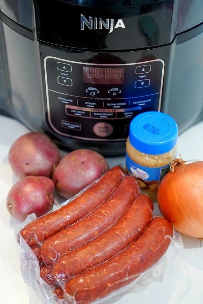 Potatoes, kielbasa sausage, an onion, and a jar of minced garlic arranged in front of a Ninja pressure cooker—solid for making flavorful air fryer sausage meals.