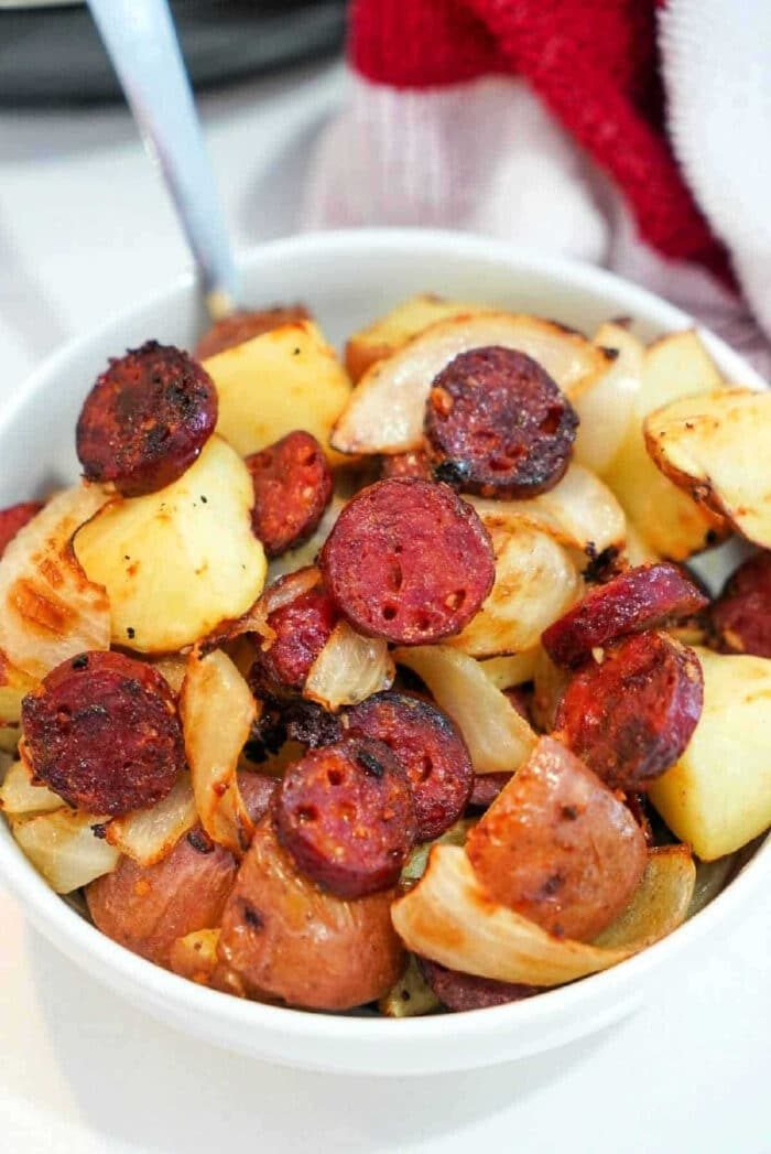 A bowl of roasted potatoes, onions, and sliced air fryer sausage, cooked and lightly browned.